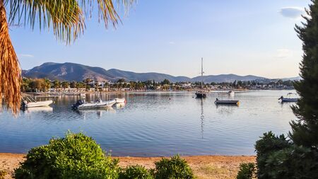 Beautiful bay with calm water, sandy beach, boats and yachts. Small town and green mountains on the coast of the Aegean seaの写真素材