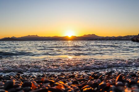 Beautiful sunset on the Mediterranean coast with islands and mountains. Stones on the beach lit by sunlight.の写真素材