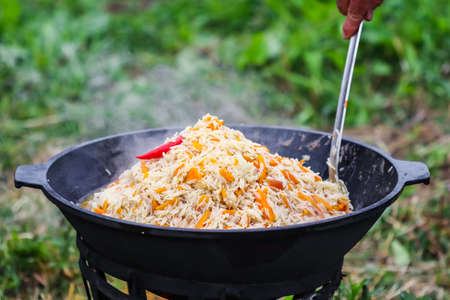 Cooking rice pilaf in a large cast-iron pot on fireの写真素材