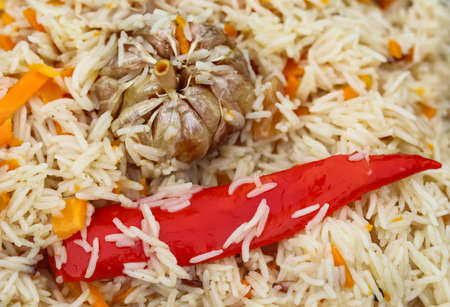 Cooking pilaf rice in a large cast iron pot over the fire. Garlic bulb and red hot pepper