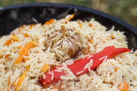 Cooking pilaf rice in a large cast iron pot over the fire. Garlic bulb and red hot pepper
