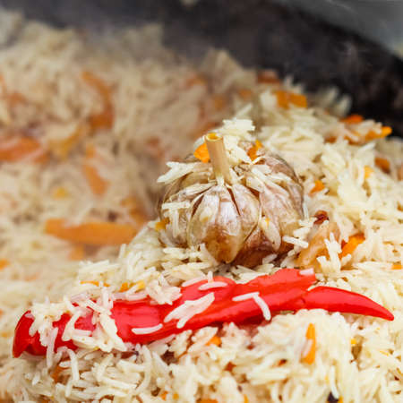 Cooking pilaf rice in a large cast iron pot over the fire. Garlic bulb and red hot pepperの写真素材