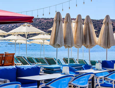 Beach umbrellas, sun loungers, tables and chairs on the shore of a calm blue sea bay in the early morning. Summer vacation and holiday destination conceptの写真素材