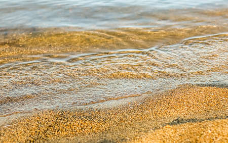Flowing wave on the sea sandy beach at sunset. Summer vacation background and coastal nature conceptの写真素材