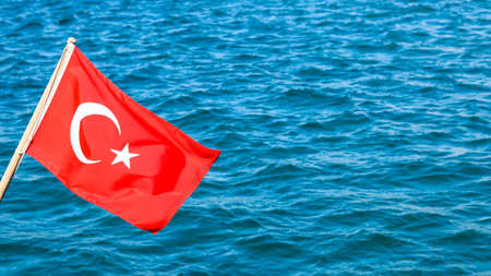 National flag of Turkey on a flagpole in the wind against a background of blue sea.の写真素材