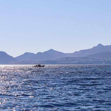 A tranquil sea with a boat, silhouetted against a hazy backdrop of distant mountains and a serene sky.の写真素材