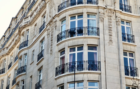 Tall elegant building facade featuring multiple stories, decorative stone carvings, traditional windows, and wrought iron balconies.の写真素材