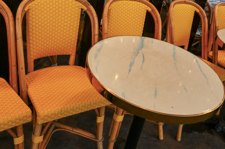 Charming Paris cafe terrace featuring iconic rattan wicker chairs and a round marble top bistro...