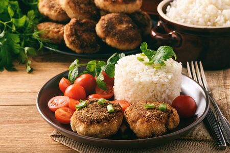 Meat cutlets with boiled rice and tomatoes on wooden background.