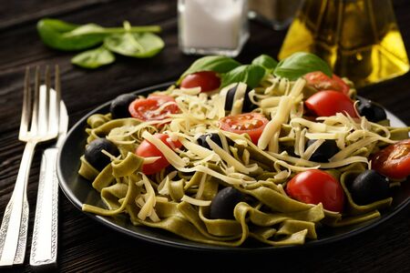 Spinach green pasta with olives, tomatoes and cheese.の写真素材