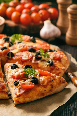 Homemade pizza with ham, cheese, tomatoes and olives.の写真素材