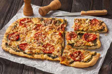 Pizza with spinach, cherry tomatoes and mozzarella on a wooden background