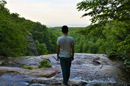 A man standing on the top of the cliff above the waterfall