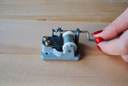 Closeup female hand holding a vintage mechanical music box with red handle on wooden plank. Put...