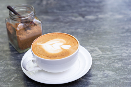 Cup of hot coffee with heart pattern in white cup and brown sugar on stone table background.の写真素材