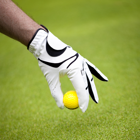 Man's hand in a white glove putting a golf ball in a golf courseの写真素材