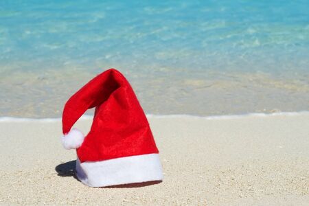 Red hat of Santa Claus on island beach with blue ocean waves on backgroundの写真素材
