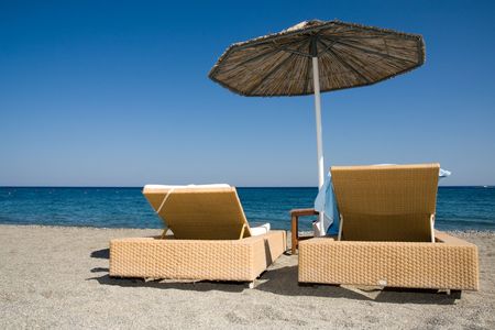 deck chairs under an umbrella on a clean beach in the hot afternoon sun.の写真素材