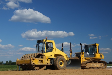 Yellow roller and bulldozer over blue sky. These machines were used to build a new road.
