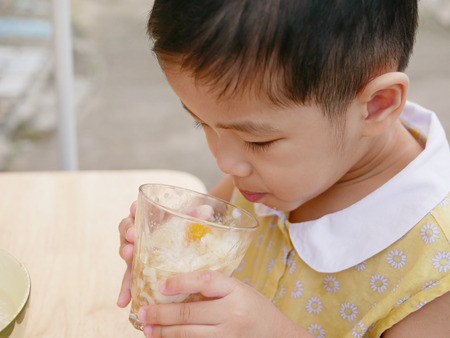 Asian baby girl enjoy trying new food by herself, soft-boiled egg (Kai Luak) - helping the baby get familiar with a challenge or trying new things in lifeの写真素材