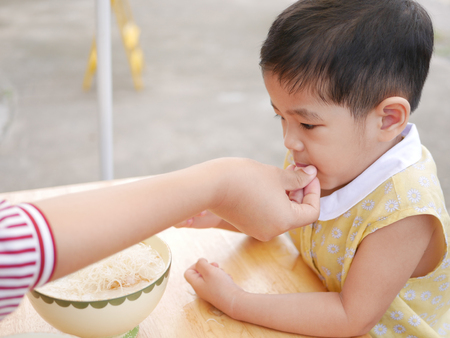 Asian mother's hand introducing a small peice of crispy deep-fried rice noodle to her little daughter for the first time - baby's development through encouraging them to try new foods / thingsの写真素材