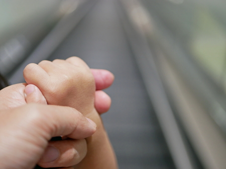 Close up of a father's hand holding a baby's hand while getting onto a moving escalator on the backgroundの写真素材