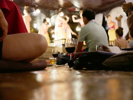 A glass of wine on the sitting floor in the mid of tourists coming to enjoy traditional NorthernThai performance and dinners, Chiang Mai, Thailandの写真素材