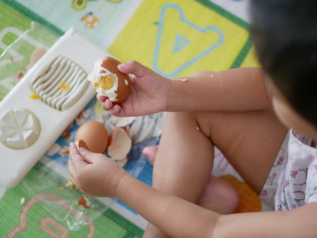 Close up of Asian baby's hands and fingers peeling boiled egg by herselfの写真素材