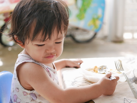 Little Asian baby girl enjoys eating food by herself - child development by allowing them to do things by themselvesの写真素材