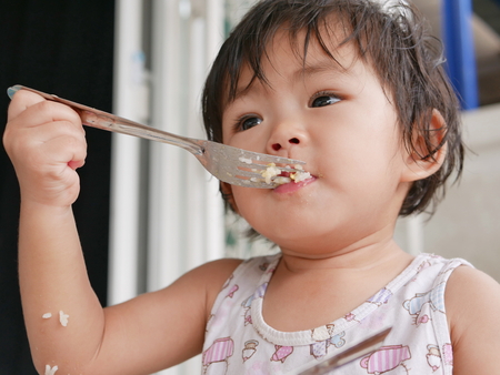 Little Asian baby girl enjoys eating food by herself - child development by allowing them to do things by themselvesの写真素材