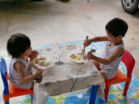 Little Asian baby girls, siblings, enjoy eating food by themselves - child development by allowing them to do things by themselvesの写真素材