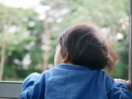 Little Asian baby girl, 18 months old, enjoys sticking her head out of a train window and having the wind whips against her faceの写真素材