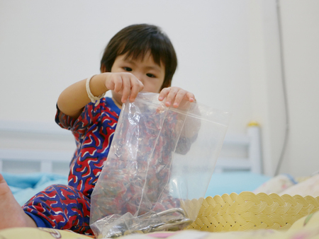 Little Asian baby girl, 17 months old, trying to close a plastic zip bag with keys insideの写真素材