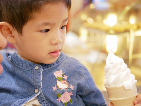 Little Asian baby being hungry for appealing ice cream cone in front of herの写真素材