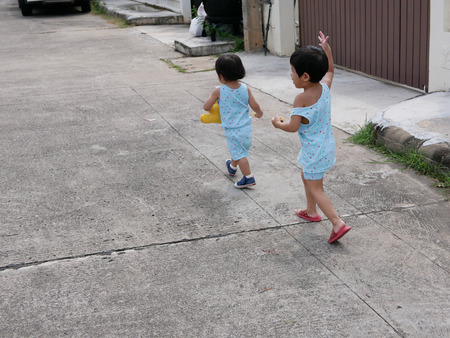 Little Asian baby girl (right) running after her little baby sister and enjoying accompanying her sister while learning and practicing to walk and runの写真素材