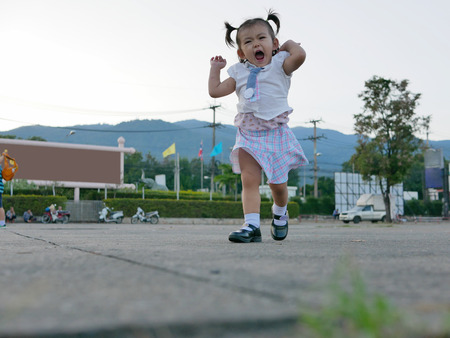 Little Asian baby girl, 19 months old, enjoys running on an outdoor concrete floorの写真素材