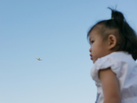 An airplane flying across the sky above little Asian baby girlの写真素材