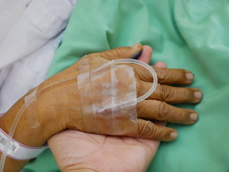 Elderly patient's hand with IV ( intravenous ) line on a supporting hand of a younger personの写真素材