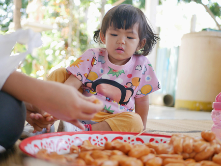 Little Asian baby girl watching her mother putting hot dogs on each wooden stick - involving baby in meal preparation creates family bonds and helps them learn life skillsの写真素材