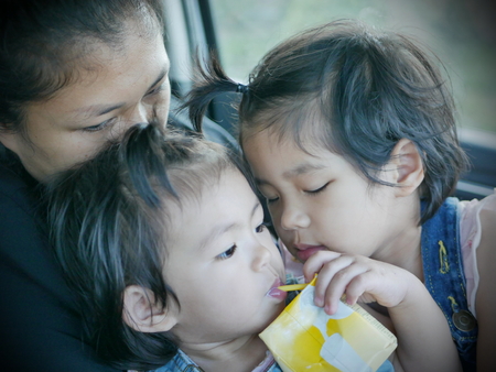 Selective focus of two little Asian baby girls, siblings, cuddling on her mother's lap in a car during a tripの写真素材