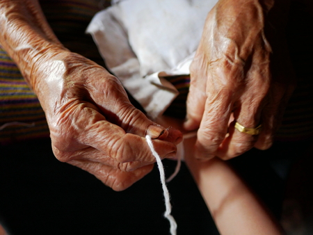 Hand of old woman waving a white string ( Sai Sin ) around her granddaughter hands - Thai traditional blessing from an elder oneの写真素材