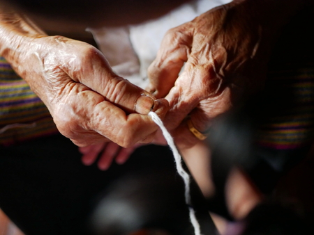 Hand of old woman waving a white string ( Sai Sin ) around her granddaughter hands - Thai traditional blessing from an elder oneの写真素材