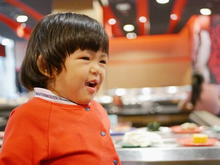 Little Asian baby girl, 25 months old, enjoys eating food / having a meal in a restaurantの写真素材