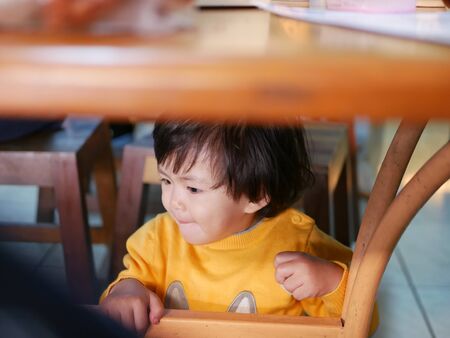 Little Asian baby girl sitting and playing / exploring under a dinning table during a meal with her...