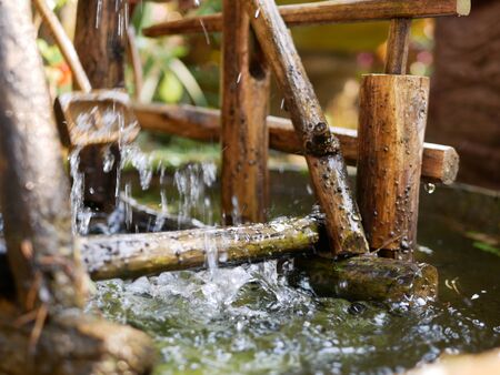 Selective focus of water drops falling from a bamboo hydraulic turbine onto a water surface and splashing in different directionsの写真素材