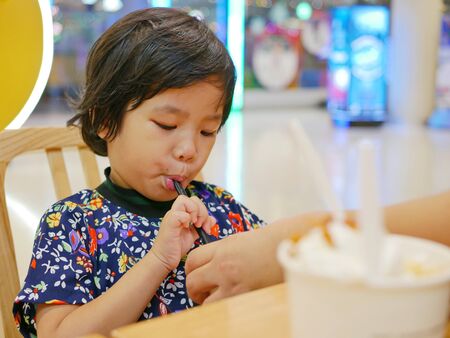 Little Asian baby girl, 38 months old, learning to sip / drink water from a big straw with help from her motherの写真素材