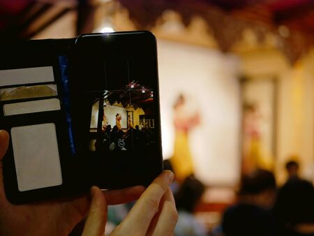 A smartphone on a tourist's hands taking a photograph of Northern Thai dancing performing on a stage