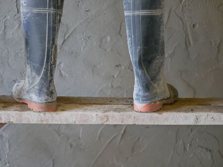 Construction worker's feet in rubber boots standing on a wooden stand while he was working,...