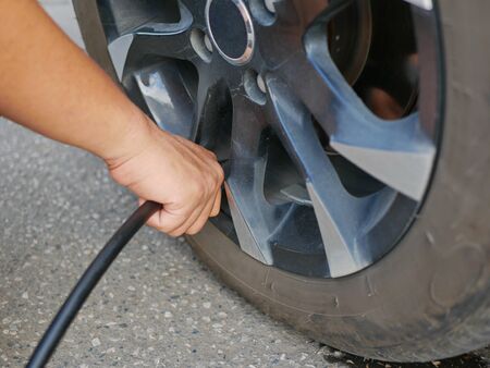 A man's hand holding an air hose and filling up a car's tireの写真素材