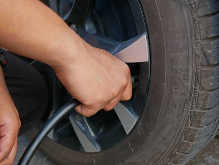 A man's hand holding an air hose and filling up a car's tireの写真素材